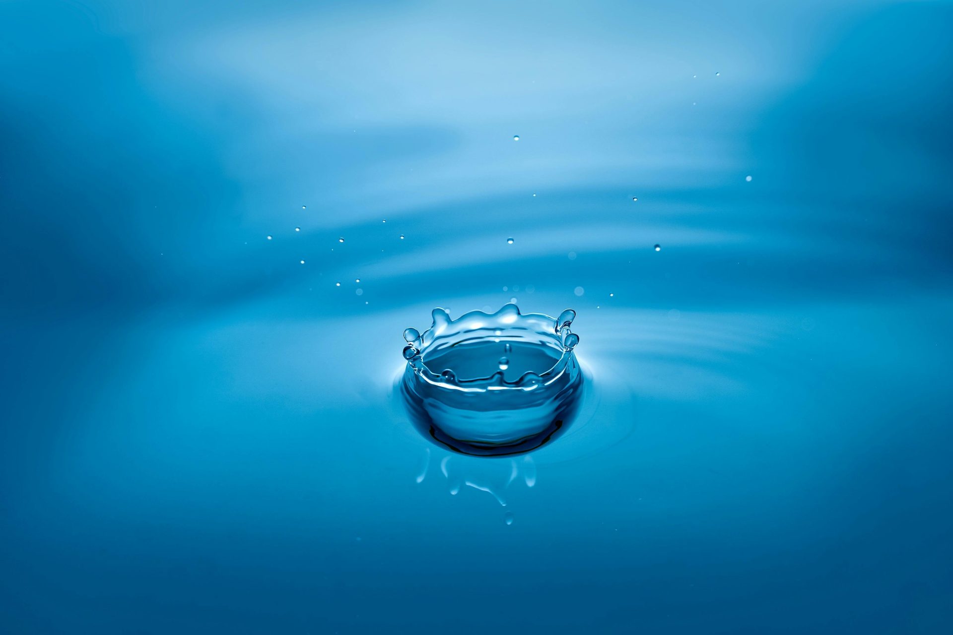 High-speed photo of a blue water droplet creating ripples and splash effects.